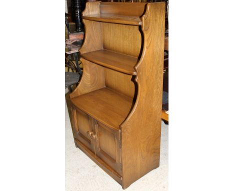 An Ercol elm bookcase cabinet of small proportions, the two graduated shelves over two cupboard doors, together with a Regenc