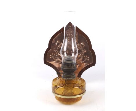 A late 19th century wall bracket with an amber glass Matador oil lamp. The later wall panel with an applied repousse copper p