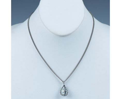 The delicate pendant is a faux pearl held by silver metal set with blue rhinestones. It is hanging on a silver metal chain th
