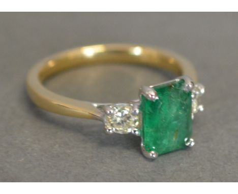 An 18ct. Yellow Gold Emerald and Diamond Ring, with a central claw set rectangular emerald flanked by diamonds within a pierc