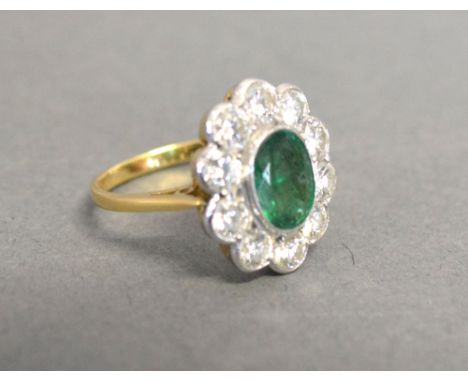 An 18ct. Yellow and White Gold Emerald and Diamond Cluster Ring with a central oval emeralds surrounded by diamonds