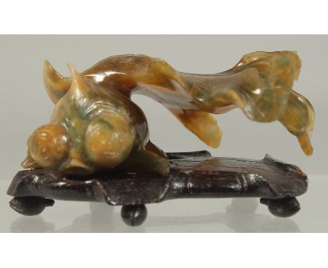 A CARVED COLOURED JADE FISH. 3ins long on a wooden base.