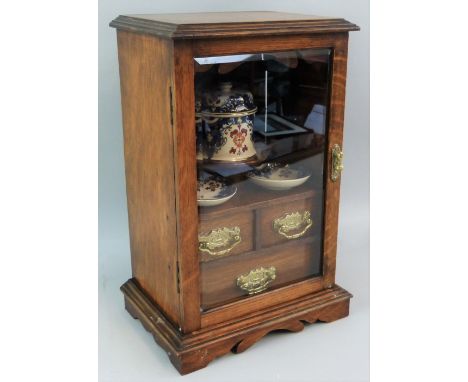 An early 20th century smoker's oak cabinet, with moulded edged top over a single bevelled glass door enclosing a fitted inter