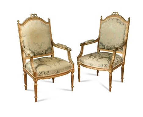 A pair of French carved giltwood fauteuils, circa 1900, the arched top rail surmounted by shaped ribbon above down swept padd