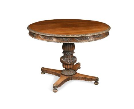 the circular tilt top with a scrolling foliate carved frieze raised on a substantial baluster column and quatrefoil base on b