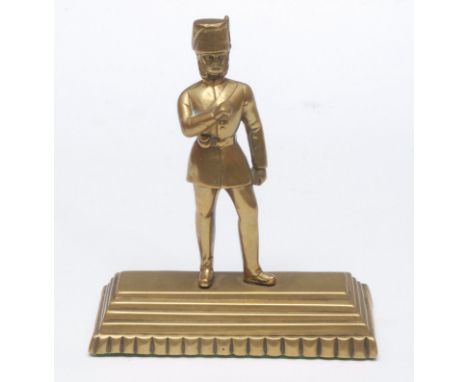 A Victorian brass desk weight, as an Hussar wearing a busby fur hat, he stands on a stepped rectangular plinth, 14.5cm high o