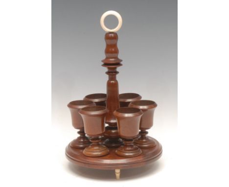 Treen - an Edwardian mahogany egg cup stand, bone carrying loop above turned column surrounded by six campana egg-cups suppor