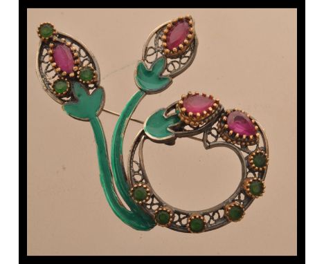 A sterling silver and enamel brooch in the form of a flower. Scrolled form with red and green stones. Weighs 15 grams.