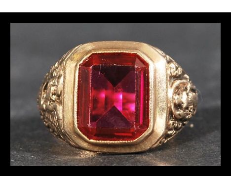 A hallmarked 9ct gold and ruby ring having a large central bezel set emerald cut&nbsp; synthetic ruby flanked by eagle and li