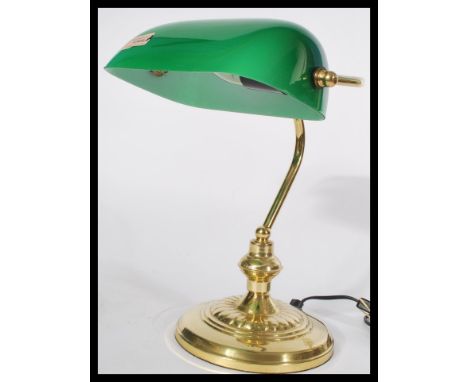 A vintage 20th century bankers desk lamp having an adjustable green glass shade raised on a brass support and circular base.