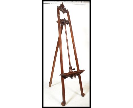 A good 20th century mahogany artists easel of tall folding form having threaded adjustable rest to centre with carved rococo 