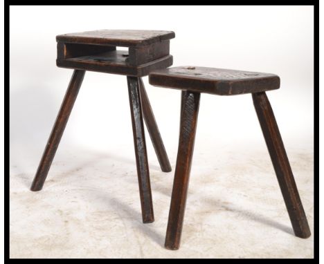 Two early 20th century oak ebonised milking stools on tripod legs with panel seats. One having open shelf recess under seat.