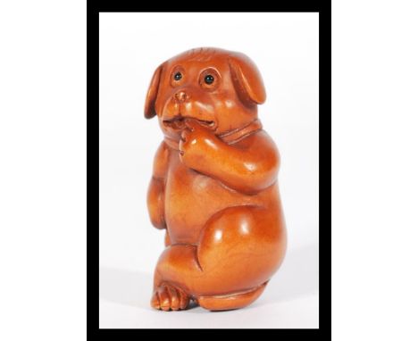 A Japanese carved wooden netsuke in the form of a dog with hand to mouth.