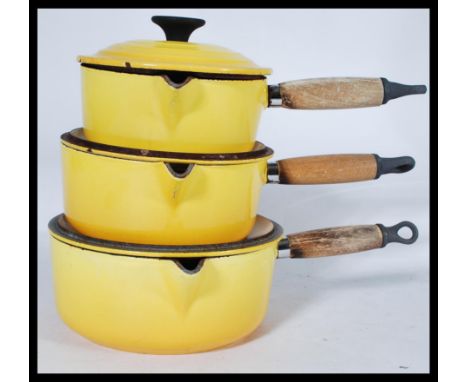 A graduating set of three French Le Creuset lidded cooking pans in an unusual yellow enamel colouring with wooden handles, Al