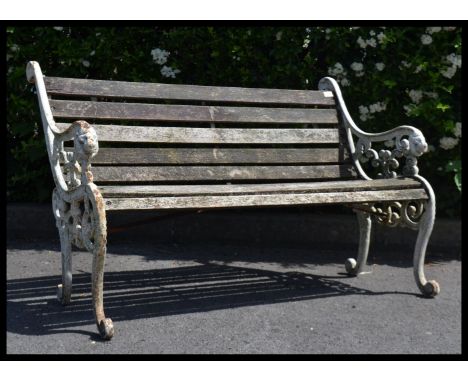 A vintage well weathered two seater garden bench seat with scrolled lions head bench ends. In the manner of Coalbrookdale.