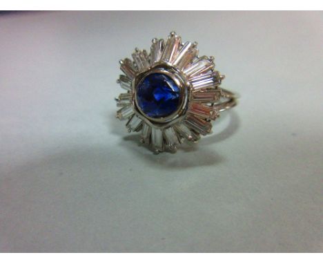 A sapphire and diamond sunburst cluster ring, the round cut light indigo coloured sapphire collet set in a splayed and undula