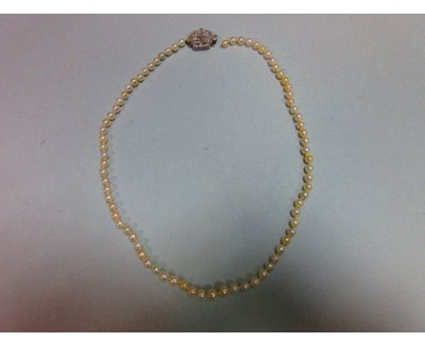 A pearl necklace with art deco diamond clasp, the individually knotted string of graduated 3.8-5.2mm pearls to a geometric do