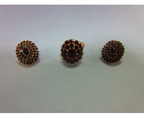A Bohemian garnet cluster ring and a pair of matched earstuds, the ring with an oval cut pyrope garnet in a double tiered bor
