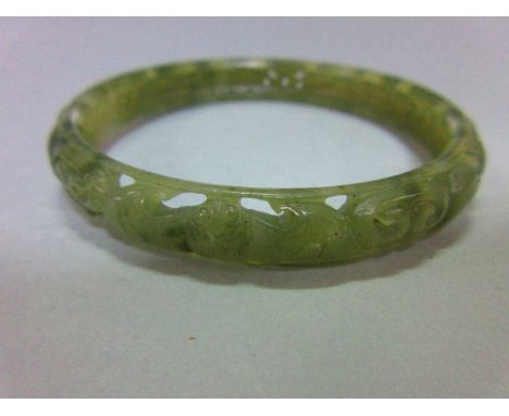 A carved jade bangle, the mottled light green jade of convex profile, pierced and carved with continuous swirling dragons, wi