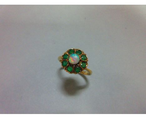 An opal and emerald cluster ring, with a round cabochon opal centre in a border of eight round cut emeralds to a plain tapere