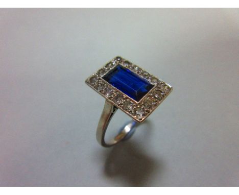 A mid 20th century sapphire and diamond ring, the rectangular step cut royal blue sapphire in a millegrain edged linear borde