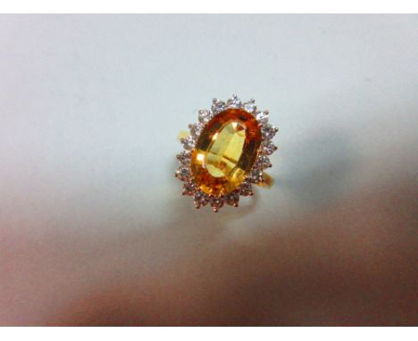 A topaz and diamond cluster ring, the oval mixed cut golden topaz claw set to a border of eighteen round brilliant cut diamon