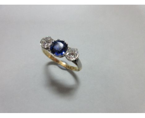 A three stone sapphire and diamond ring, claw set with a round cut royal blue sapphire between old cushion cut diamonds, in w