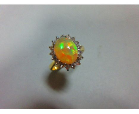 An opal and diamond cluster ring, the oval cabochon opal, displaying vivid predominently green and orange fire, in a border o