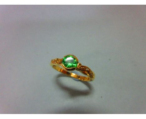 An 18ct gold ring set with a green garnet and diamond highlights, the bright apple green round cut garnet half collet set bet