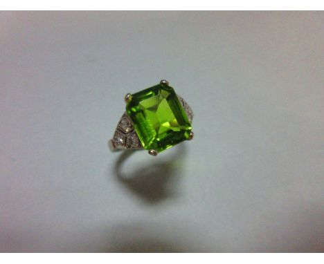 A 1930s style peridot and diamond ring, the emerald cut peridot measuring 10.6 x 8.7mm, four claw set to tapered shoulders se