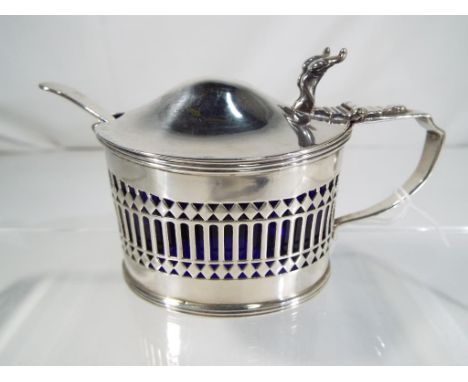 An Edward VII silver hallmarked mustard pot of oval form with pierced decoration with blue glass liner and silver spoon, Ches