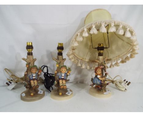 A pair of Goebel Hummel figural lamp bases depicting a boy sat in an apple tree and a further Goebel Hummel lamp base depicti