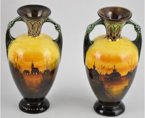 A near-pair of Continental Art Nouveau glazed ceramic twin handled vases, decorated with buildings silhouetted at sunset, H. 