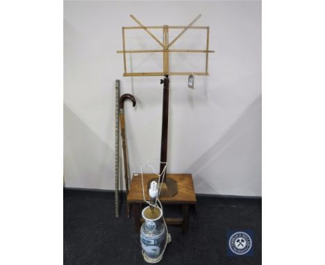 An early 20th century music stand on metal base, pottery table lamp, walking stick, yard stick and a pine stool 