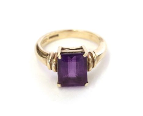 A 9 carat gold amethyst ring, the emerald-cut amethyst in a yellow four claw setting, to a tapered shoulder plain polished sh