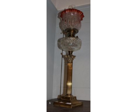 A Victorian brass Corinthian columnar oil lamp with clear glass reservoir and cranberry shade 