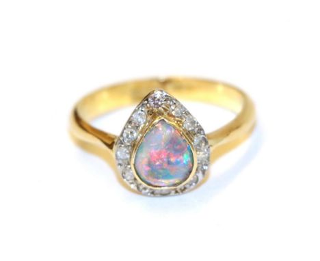 An 18 carat gold black opal and diamond cluster ring, the pear shaped black opal in a yellow collet setting, within a border 