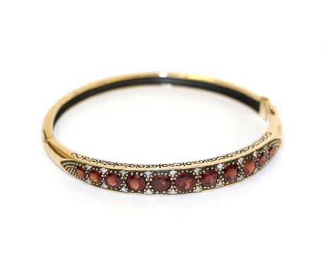 A 9 carat gold garnet and diamond hinged bangle, the eleven graduated garnets with eight-cut diamond accents, in yellow claw 