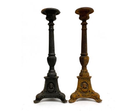 A pair of cast iron candlestick holders on tapering columns, the tripod base with mask decoration, each 42.5cmH 