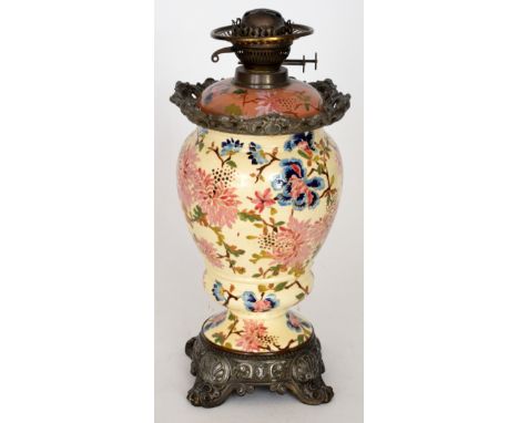 A late 19th Century over painted pottery baluster form oil lamp decorated with chrysanthemums on an ivory ground to a scroll 