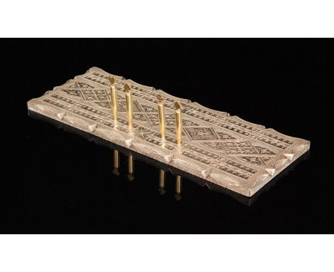 A modern hallmarked silver cribbage board, the shaped rectangular board centred by cast foliate panels within an interlaced g