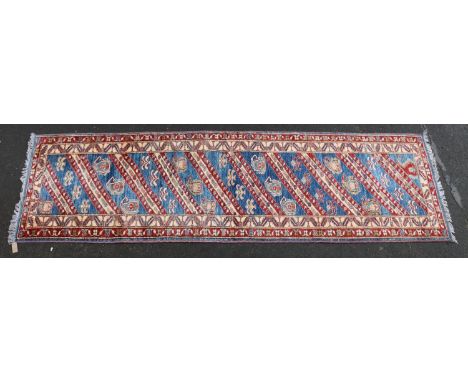 Kazak style runner, polychrome geometric motifs and stripes on a blue ground within conforming borders, 300cm x 90cm. 
