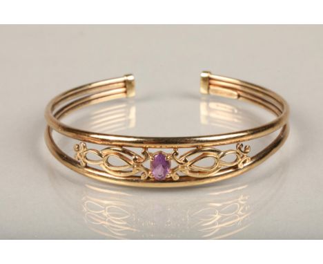 9ct gold bangle, set with an oval cut amethyst on a scrolled open work mount between a split band, interior W5.5cm, 7.1g. 