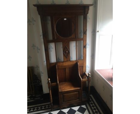 20th century oak hallstand having central circular mirror above settle style seat with hinged storage space, flanked by stick