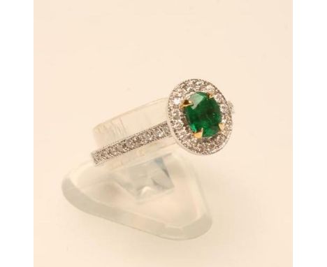 AN EMERALD AND DIAMOND CLUSTER RING, the oval facet cut Colombian emerald claw set to a border of numerous small millegrain s