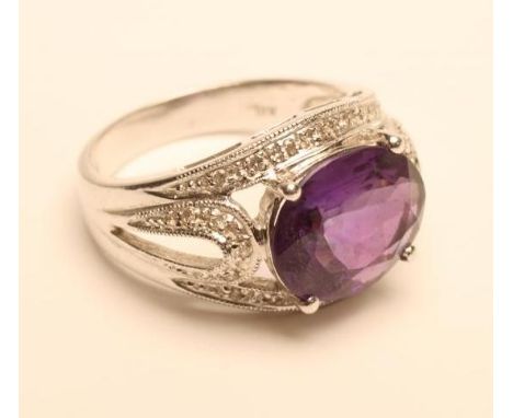 AN AMETHYST AND DIAMOND COCKTAIL RING, the oval facet cut amethyst claw set to a border and open shoulders millegrain set wit