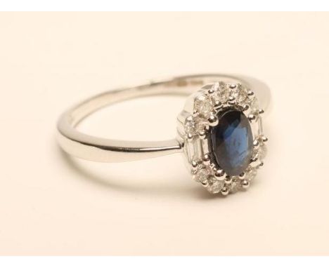 A SAPPHIRE AND DIAMOND CLUSTER RING, the oval facet cut sapphire claw set to a border of ten small brilliants and two baguett