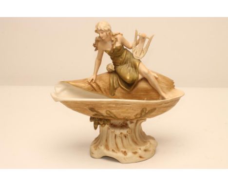 AN ART NOUVEAU ROYAL DUX BISQUE PORCELAIN FIGURAL CENTREPIECE, modelled as a young maiden holding a harp, seated on the edge 