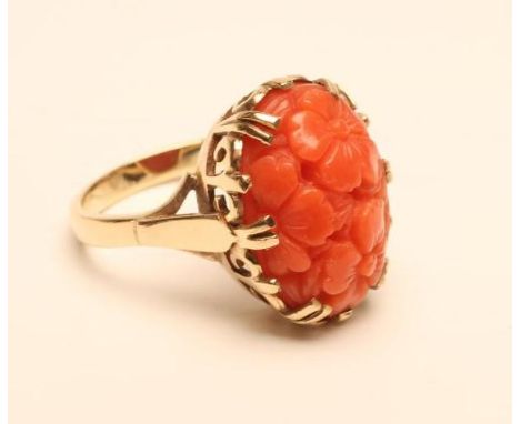 A DRESS RING, the oval coral panel carved and pierced with flowerheads on a plain 9ct gold shank, size M 1/2    (Est. plus 18