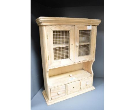 A small pine wall cabinet, having a moulded cornice over two hinged doors with metal mesh inserts with open section and three